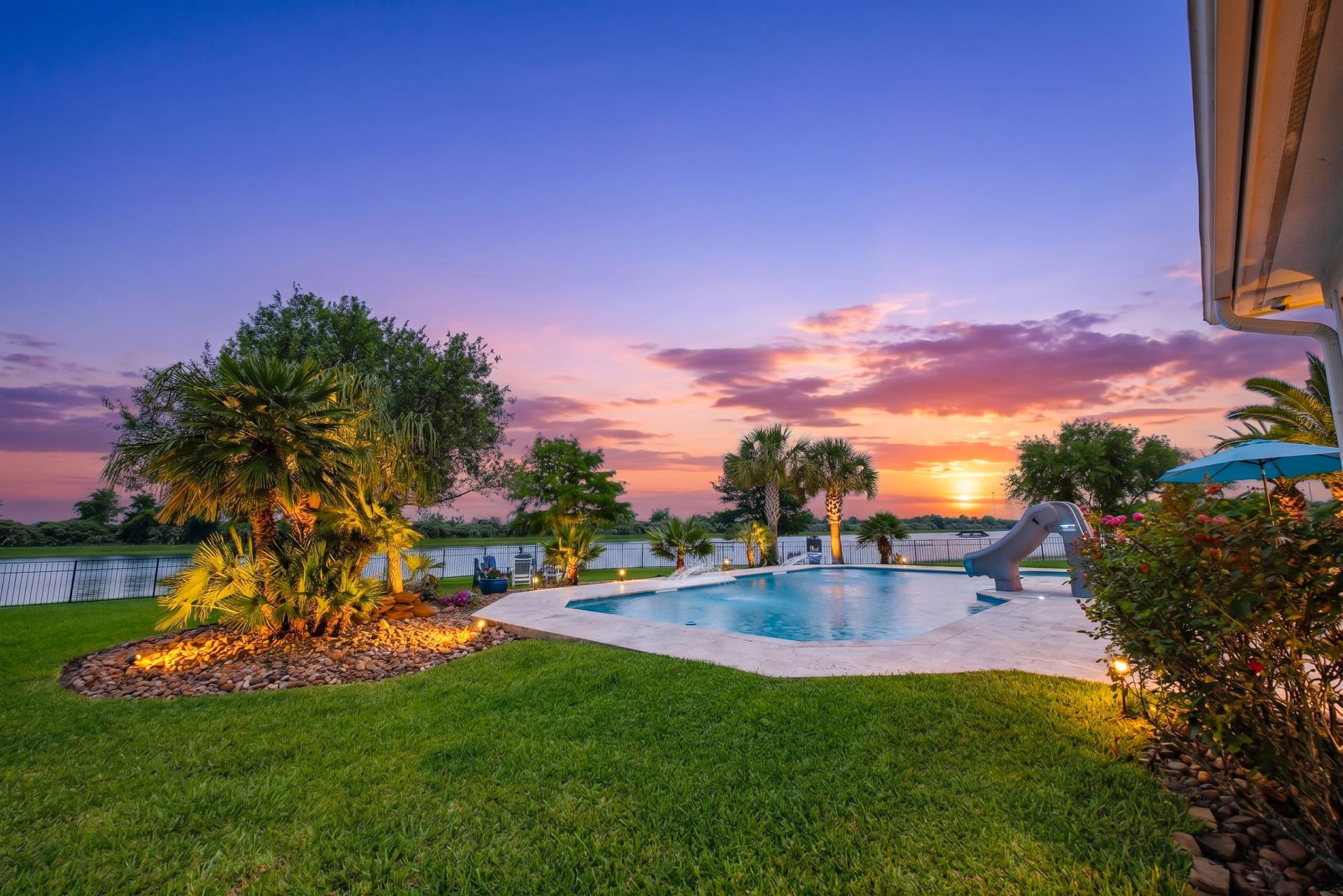 Sunset over a private ski lake behind a lit pool and palm-lined backyard in Lago Santa Fe